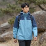 아이더 모멘텀 플렉션 2.5L 방풍 자켓을 입고 산책하는 모습. 스카이블루와 카본 컬러의 세련된 디자인.