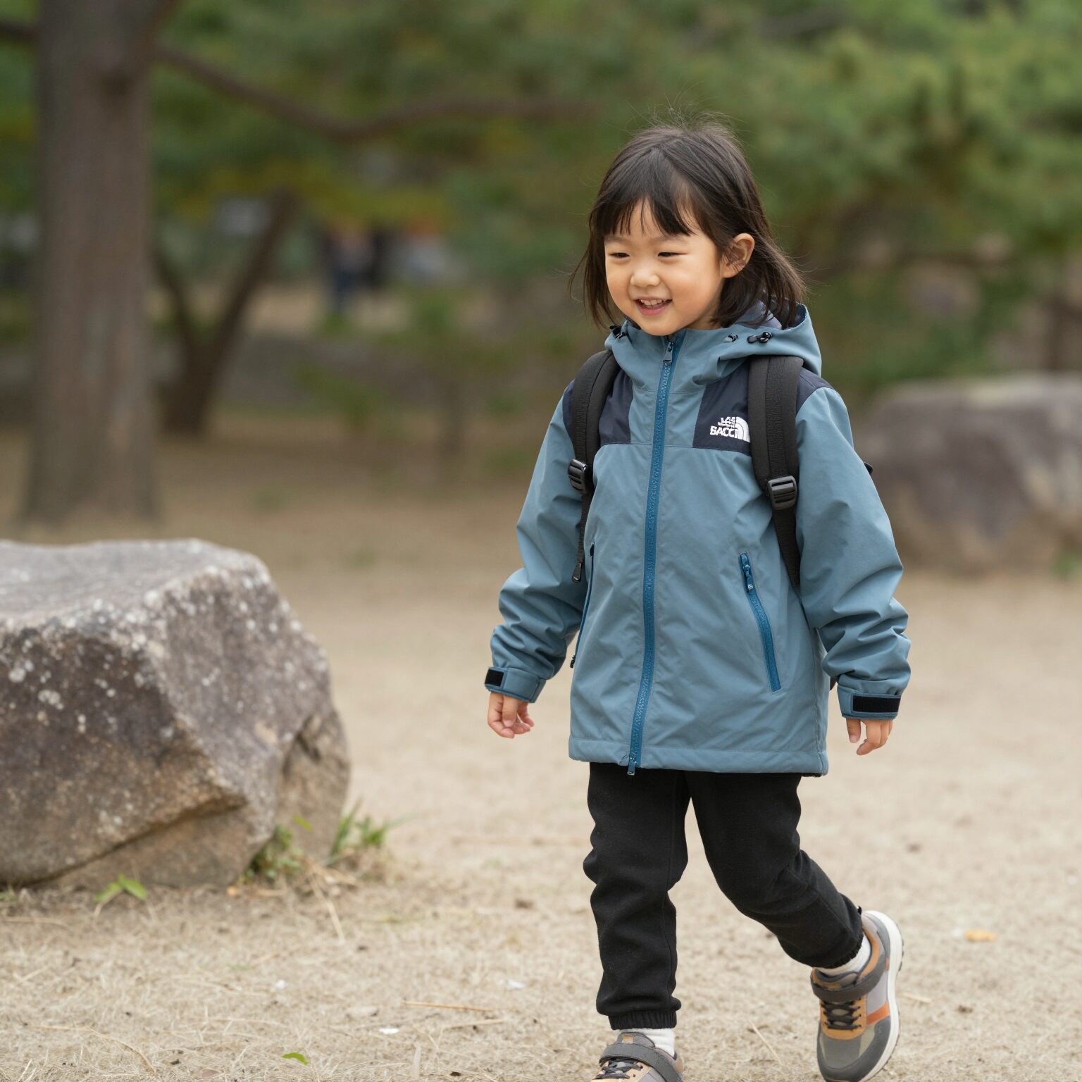 노스페이스키즈 시티 칠러 자켓을 입은 여아가 공원에서 웃고 있는 모습