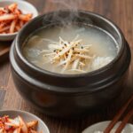 완성된 들깨 쑥국이 담긴 뚝배기와 밥과 김치가 함께 있는 모습