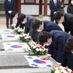 한국 현충일 추모식에서 국립묘지를 방문한 사람들이 묵념하고 있는 모습. 태극기와 국화꽃이 배치되어 있다.