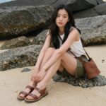 김나영 샌들 10년째 애용하는 이유 김나영이 솔트워터 샌들을 신고 해변에서 포즈를 취한 모습. 브라운 스트랩 디자인이 자연스럽게 어우러진 여행룩
