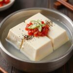 두부와 두유로 만든 콩국수 그릇 위에 오이와 방울토마토 고명이 올려져 있고 통깨가 뿌려져 있다
